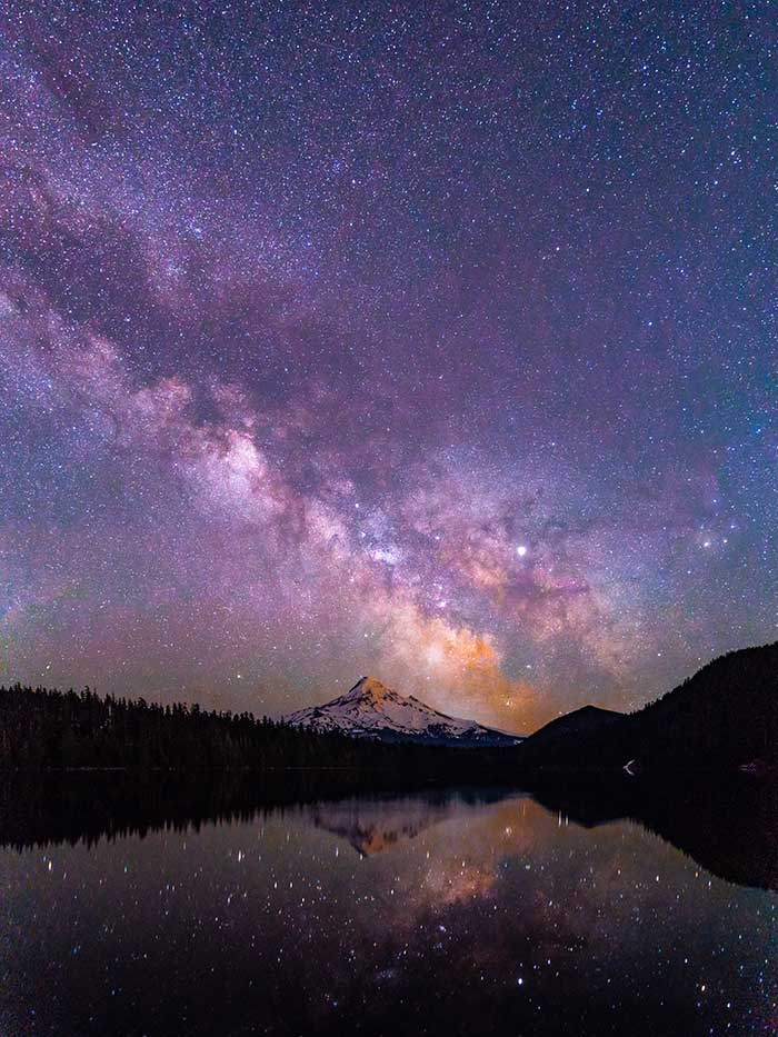 a lake with a mountain in the background under a night sky filled with stars